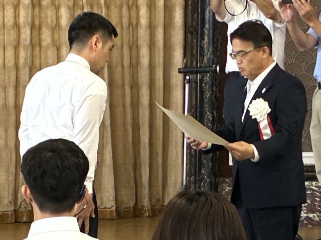 賞状を受け取る様子の写真。左手に山本選手、右手に大村知事。