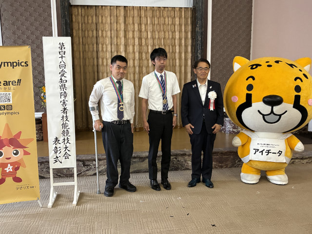 受賞した2名がメダルを首に掛け、大村知事とマスコットの「アイチータ」と一緒に記念撮影した様子の写真。左から山本選手、小木曾選手、大村知事、アイチータ。